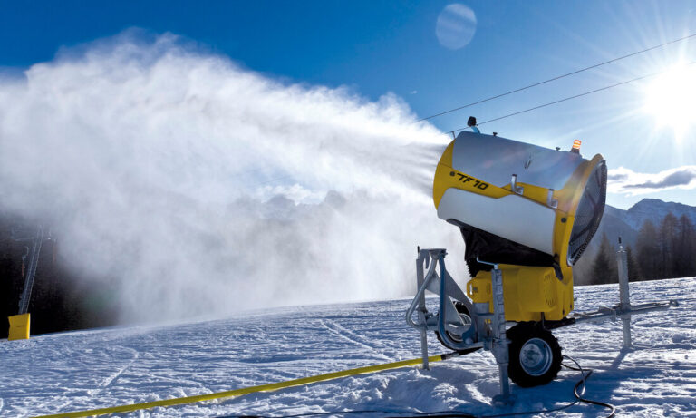 Snowmaking: fan and lance guns creating snow under cold, dry night conditions near a ski slope
